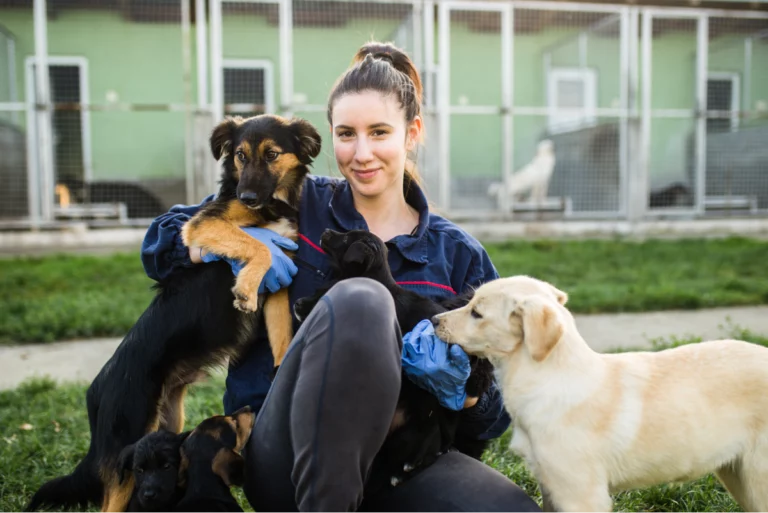 Woman posing with two dogs in front of kennel smiling