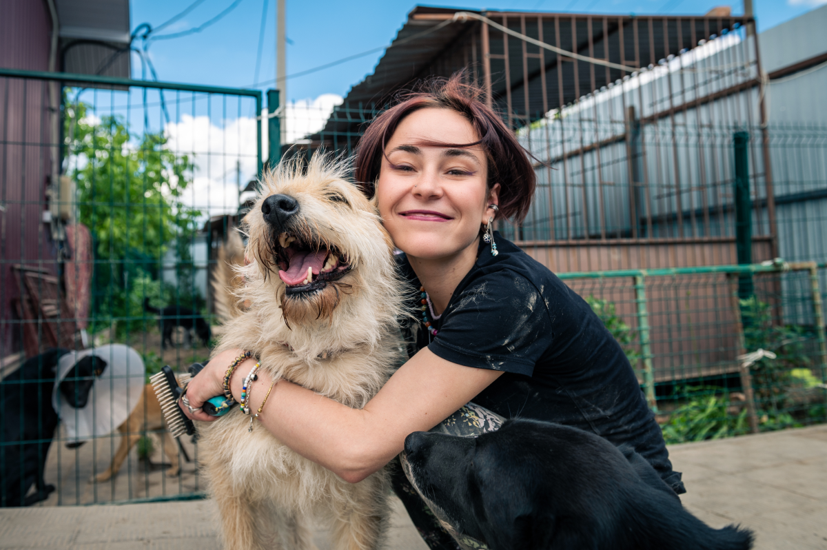 Happy animal shelter worker hugging a smiling dog in an outdoor kennel.