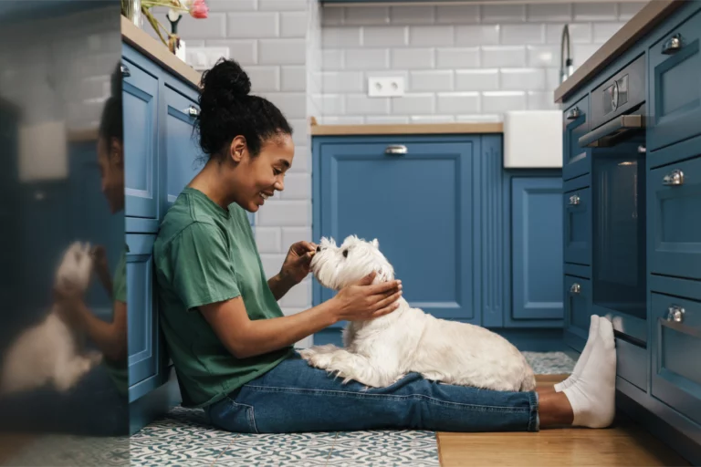 Pet sitter sitting on kitchen floor with small dog in her lap