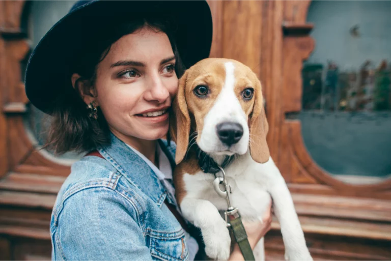 Dog walker on the street holding up a beagle on a leash.