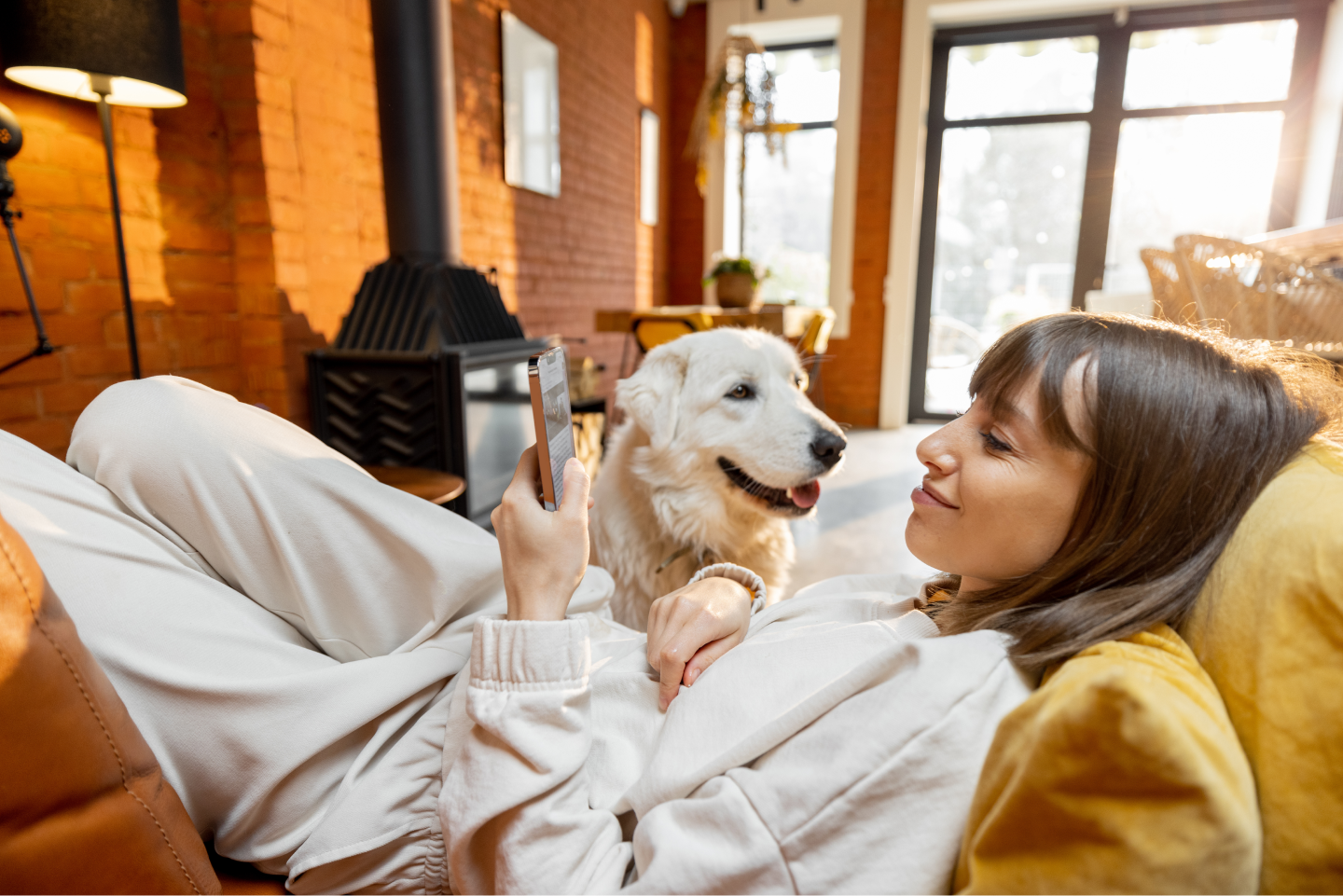 Pet professional lying down in a cozy home and using a phone with a white Labrador close by.