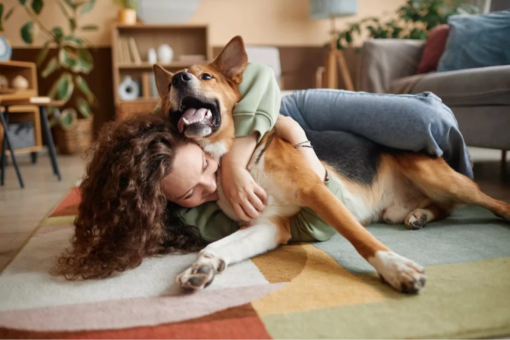 Pet sitter snuggles a happy dog on the floor in a client's home.