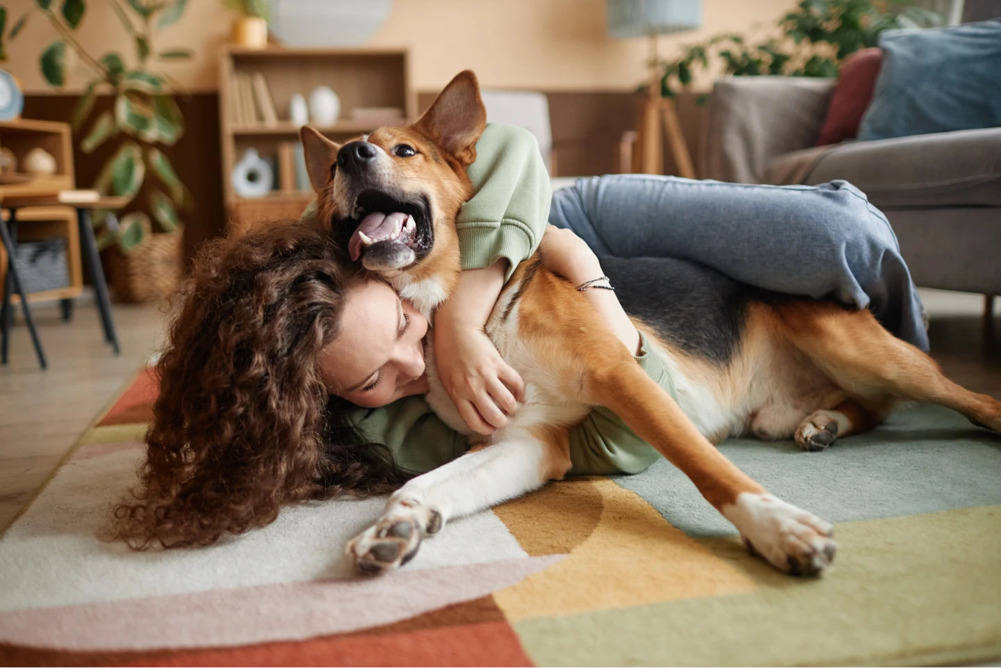 Pet sitter snuggles a happy dog on the floor in a client's home.