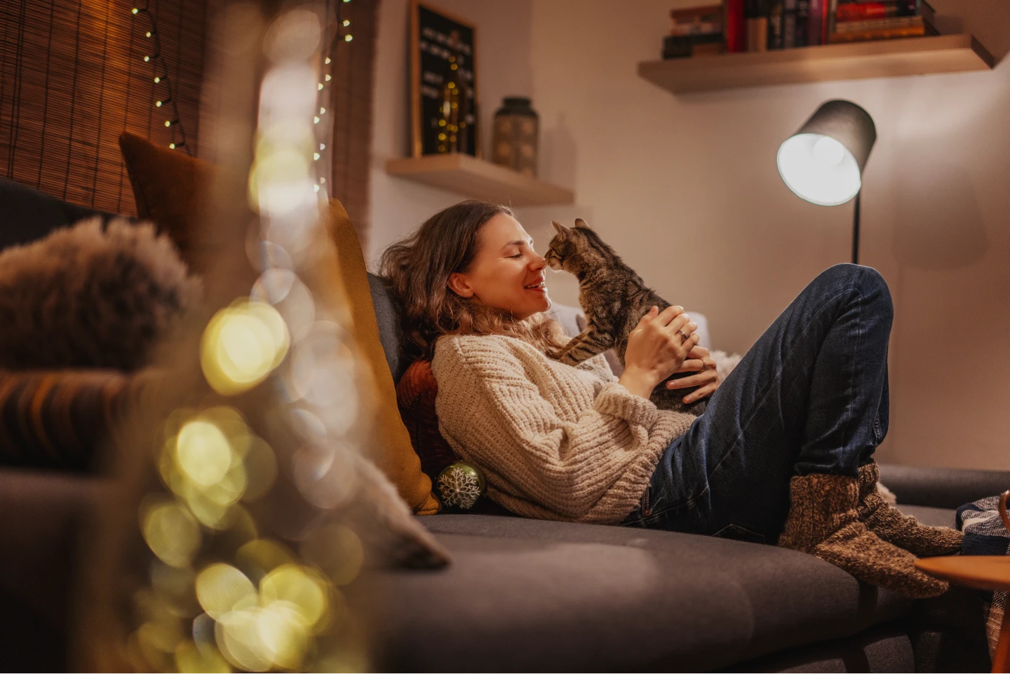 A pet care professional cuddling with a cat in a home on a cozy winter evening around the holidays.